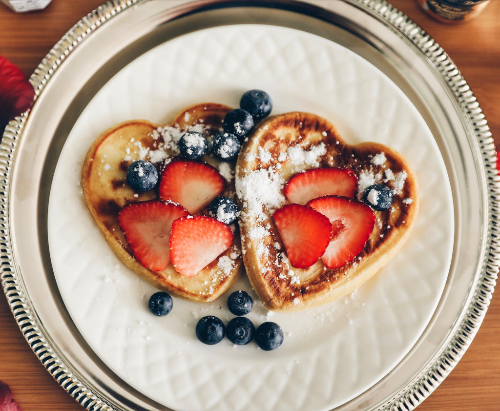 heart-shaped pancakes covered with strawberries blueberries and sugar powder