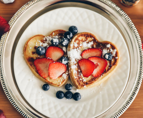 Image of heart-shaped pancakes covered with strawberries blueberries and sugar powder
