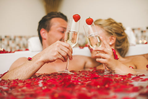 happy couple taking a romantic bath with rose petals and drinking champagne