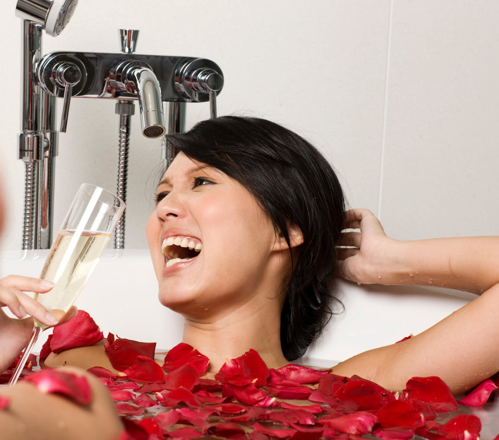 happy woman in a bathtub with rose petals drinking champagne